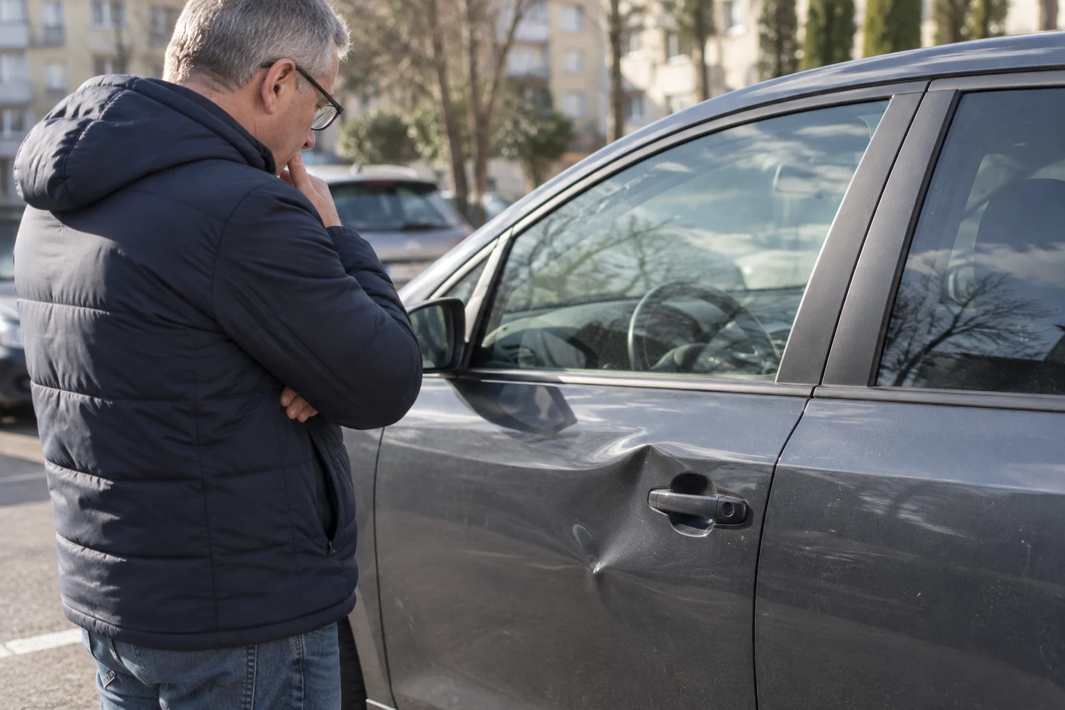 Žmogus iš atstumo apžiūri įlenktas automobilio duris jų neliesdamas.