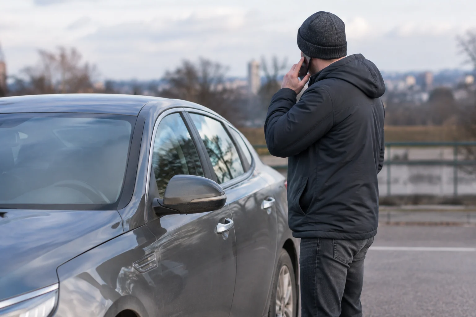 Žmogus kalbasi telefonu šalia stovinčio automobilio.