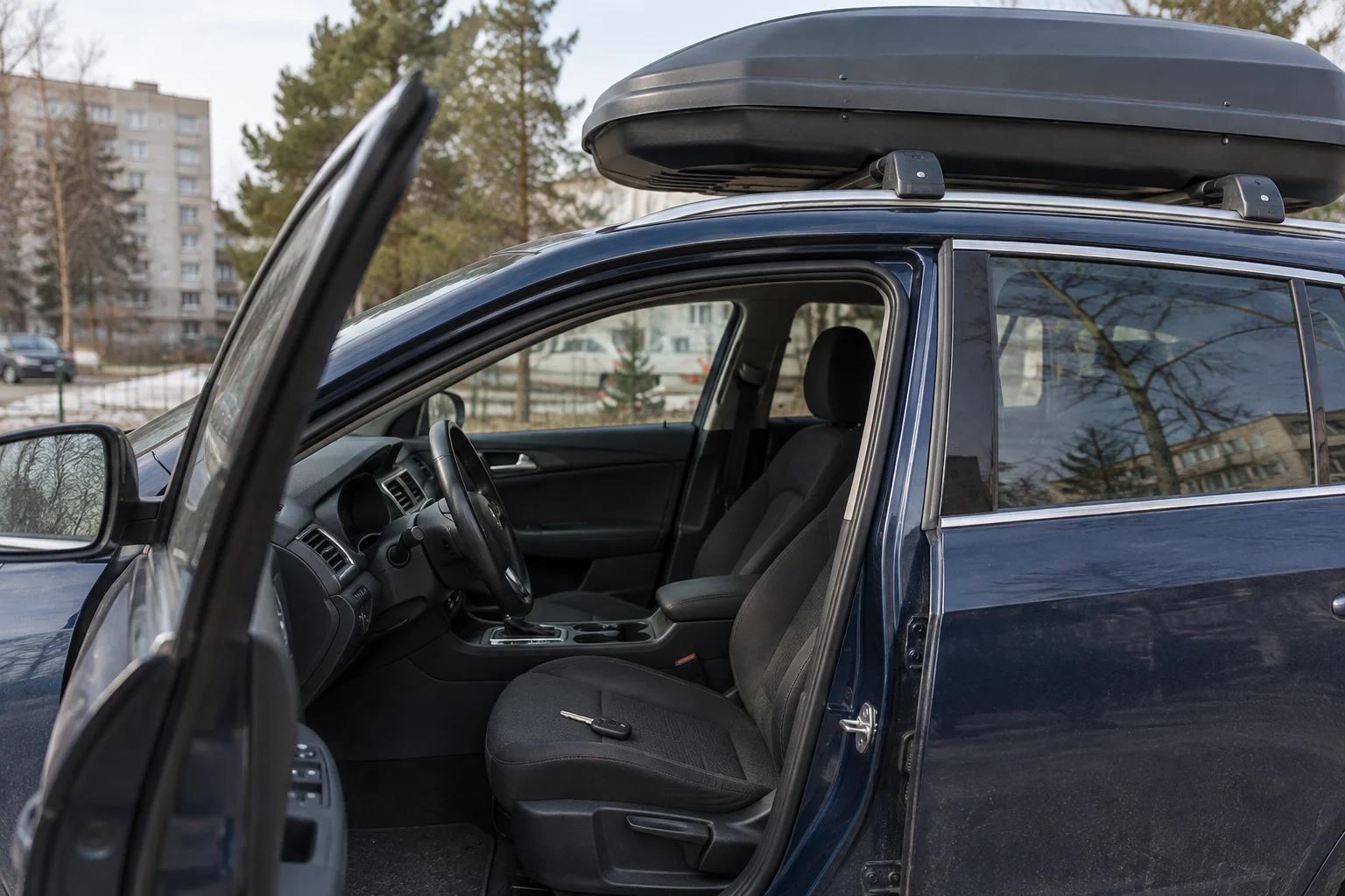 Pro atidarytas automobilio duris matomas ant sėdynės gulintis raktas, o viršuje – uždara stogo bagažinė.